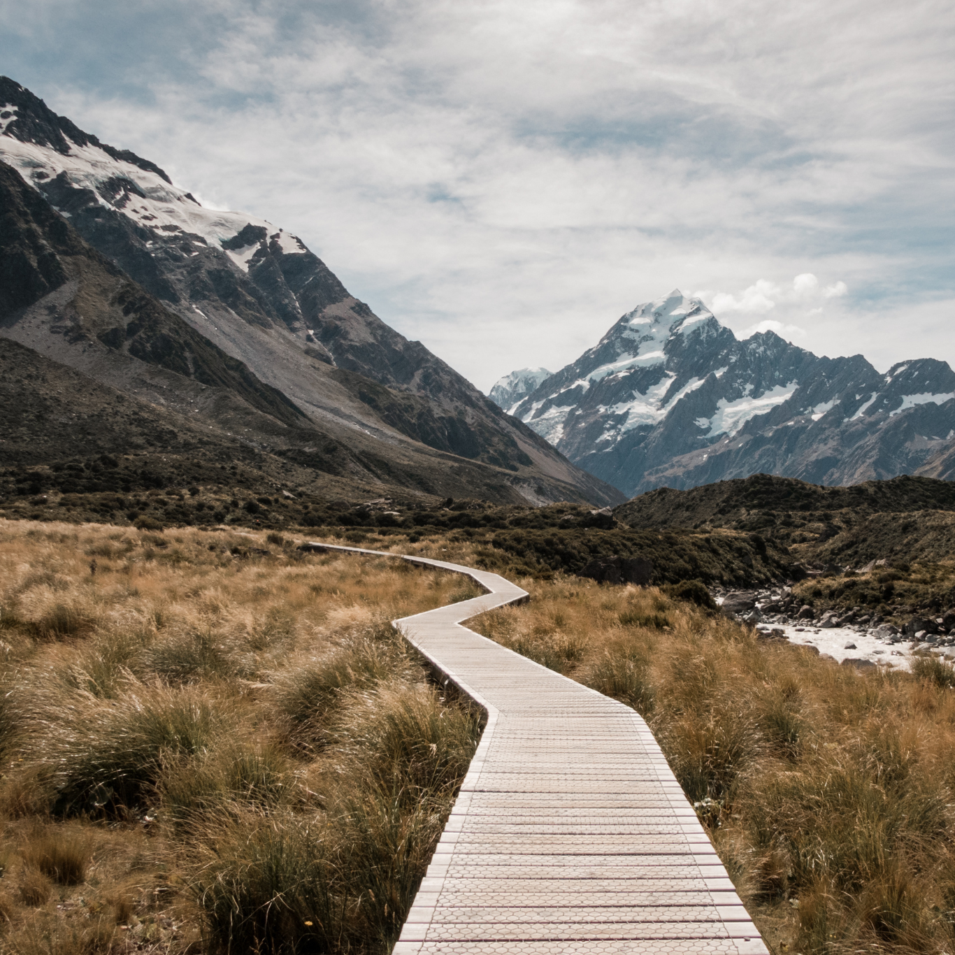 Image of a path leading one way towards some mountains in a field on a wooden bridge path