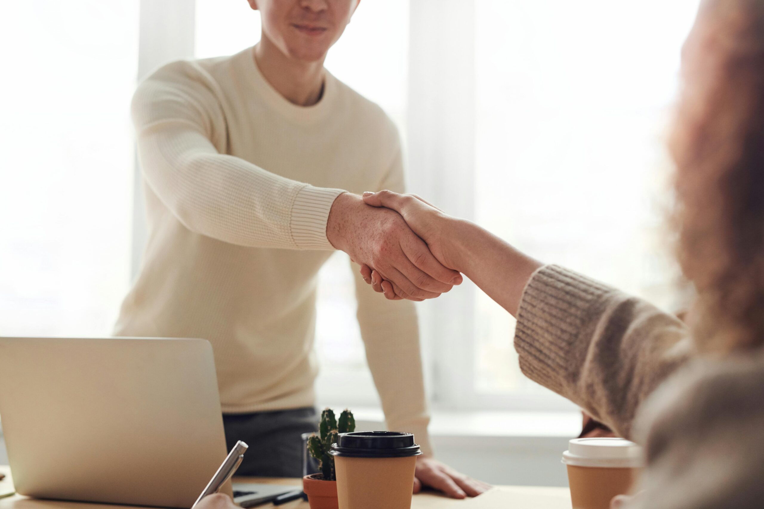 A professional handshake between two people at a meeting table, symbolizing partnership and trust.